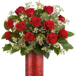 Red roses arranged in a red vase with white filler flowers