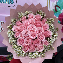 Bouquet of pink roses with small white filler flowers wrapped in pink paper