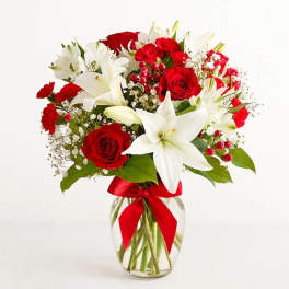 Red roses and white lilies in a glass vase with a red ribbon