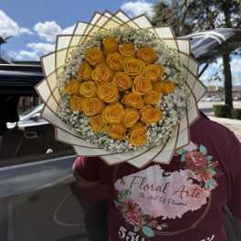 Bouquet of yellow roses with white filler flowers wrapped in layered paper