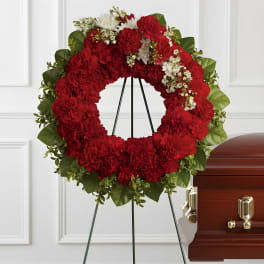 Red floral funeral wreath on a stand beside a casket