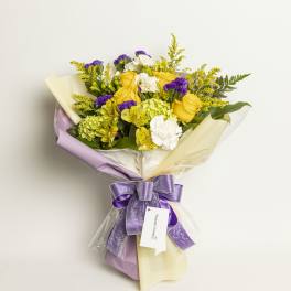Yellow roses and white flowers in a wrapped bouquet with a purple ribbon