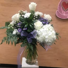 White rose and hydrangea bouquet in a glass vase with purple ribbon