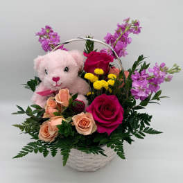Pink teddy bear in a basket with roses and purple flowers
