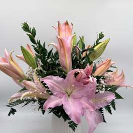 Pink lilies arranged in a white vase with greenery