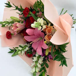 Bouquet of pink lilies, red carnations, and peach roses wrapped in blush paper