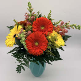 Bright red and yellow gerbera daisies with snapdragons in a teal vase