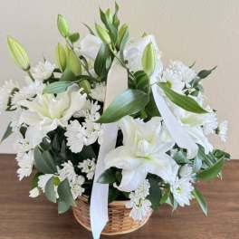 White lilies and daisies arranged in a wicker basket with a white ribbon