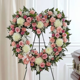 Heart-shaped floral wreath with pink roses and white blooms on a stand