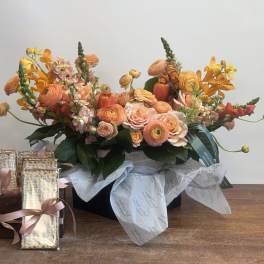 Low peach and orange flower arrangement in a black hatbox beside a wooden crate of ribbon-tied crackers.