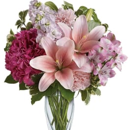 Pink lilies with mixed pink and white blooms arranged in a clear glass vase