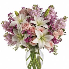 Arrangement of white lilies, pale pink roses and purple flowers in a clear glass vase