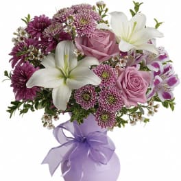 Lavender and white bouquet with lilies, roses, and mums in a light purple vase with ribbon bow