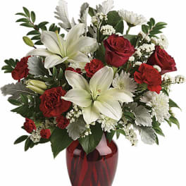 Red and white arrangement with lilies, roses, carnations, and mums in a red glass vase