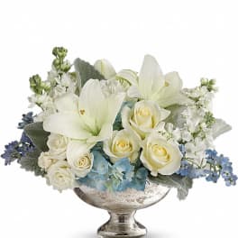 Low arrangement of white lilies and roses with blue flowers in a silver pedestal bowl