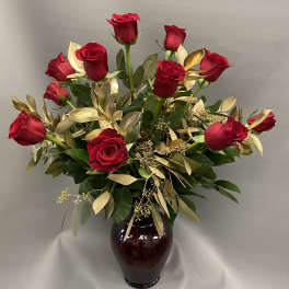 Arrangement of red roses with gold foliage in a dark red glass vase