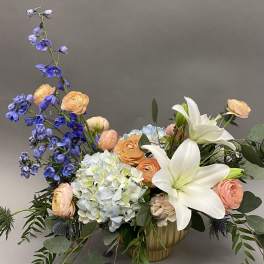 Mixed bouquet with white lilies, blue delphinium, peach ranunculus, and pale hydrangea