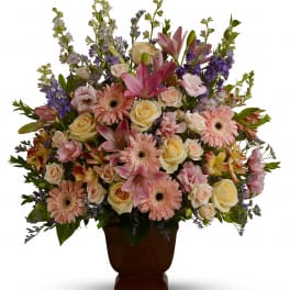 Large pastel arrangement of pink lilies, gerberas, and roses in a brown pedestal vase