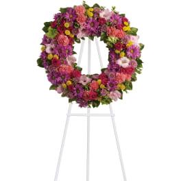Bright pink and purple floral wreath with yellow accents displayed on a white metal easel
