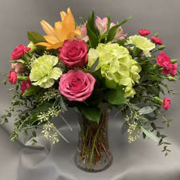 Mixed bouquet of pink roses, green hydrangea, and an orange lily in a clear glass vase