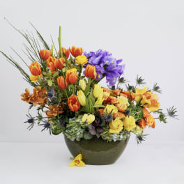 Colorful bouquet of tulips, roses, and orchids in a dark vase