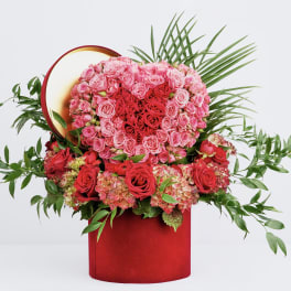Heart-shaped rose arrangement in a red box with greenery