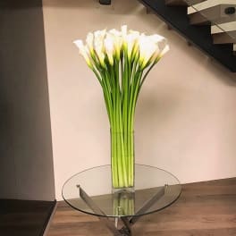 Tall vase of white calla lilies on a glass table