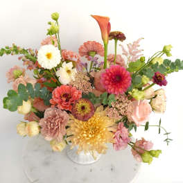 Mixed bouquet of pink, peach, yellow, and white flowers in a white vase