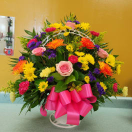 Colorful mixed flower arrangement with a pink ribbon on a white stand