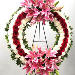 Standing floral wreath with pink lilies, red roses, and white flowers on an easel
