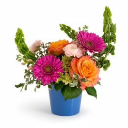 Bright arrangement of pink gerbera daisies and orange roses in a blue pot