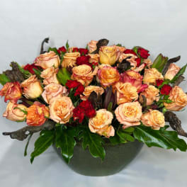Peach and red roses arranged in a low dark bowl