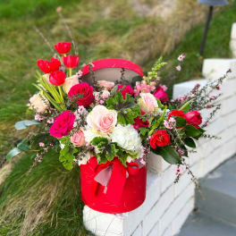 Red and pink roses arranged in a red hatbox with ribbon