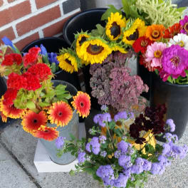 Assorted colorful flower buckets with sunflowers, gerbera daisies, and purple blooms