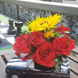 Red roses and yellow sunflowers arranged in a black truck-shaped vase