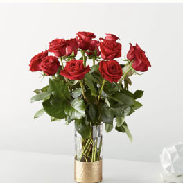 Tall arrangement of red roses in a clear glass vase with a gold base