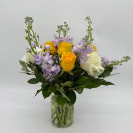 Bouquet of yellow and white roses with lavender flowers in a glass vase