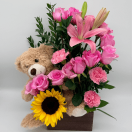 Pink roses and lilies arranged with a teddy bear and sunflower in a wooden box