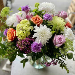 Mixed arrangement of roses, chrysanthemums, and carnations in a clear glass vase