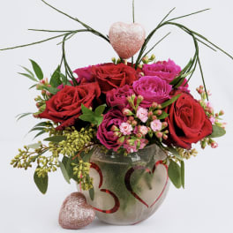 Red and pink roses in a heart-decorated vase with glittery heart accents