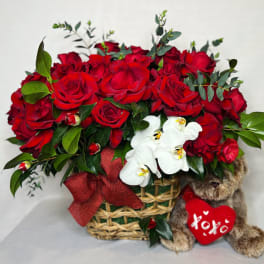 Red roses in a basket with white orchids and a teddy bear holding a heart