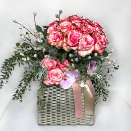 Pink roses and orchids in a woven basket with ribbon