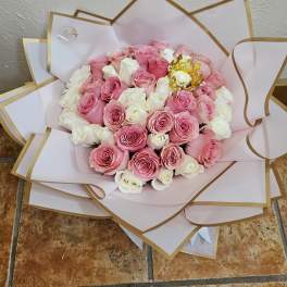 Bouquet of pink and white roses wrapped in white paper with gold trim