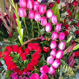 Basket arrangement of pink and red roses with lilies and greenery