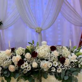 White floral wedding backdrop with draped fabric and a matching flower-covered table