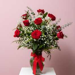 Red roses in a glass vase with baby's breath and a red ribbon