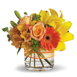 Bouquet of yellow lilies, orange roses, and a gerbera daisy in a glass vase