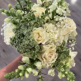 Cream roses and white flowers in a hand-held bouquet with variegated greenery.