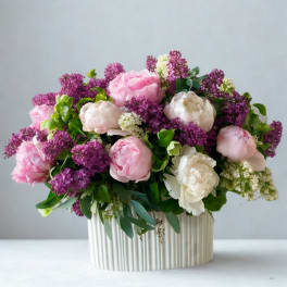 Pink and white peonies with purple lilac in a ribbed cream vase