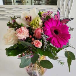 Mixed pink and white flower arrangement with a faux butterfly in an iridescent glass vase